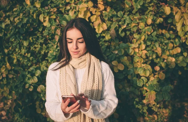 Nő használ smartphone őszén. Őszi lány szúró telefon beszélgetést nap fáklyát lombozat. Kaukázusi modell erdő őszi színekkel portréja — Stock Fotó