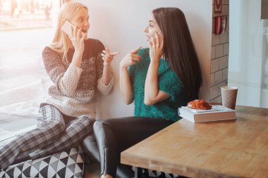 Dostluk ve teknoloji. Akıllı telefonlar kafede çay veya kahve yudumlarken kullanarak iki güzel kızlar.