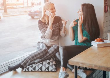 Dostluk ve teknoloji. Akıllı telefonlar kafede çay veya kahve yudumlarken kullanarak iki güzel kızlar