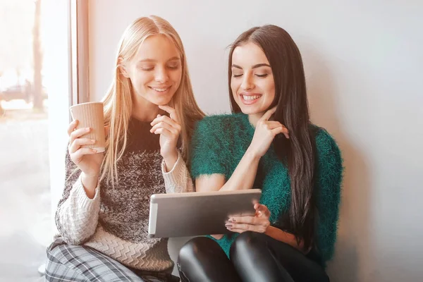 Zwei junge Frauen unterhalten sich in einem Café. zwei Freunde beim gemeinsamen Kaffee. ein Mädchen benutzt ein Tablet. — Stockfoto