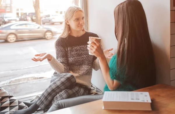 Dos mujeres jóvenes charlando en una cafetería. Dos amigos disfrutando del café juntos . — Foto de Stock