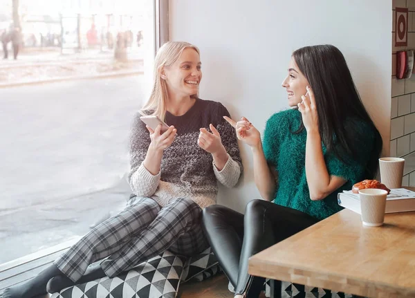 Amizade e tecnologia. Duas meninas bonitas usando smartphones enquanto bebem chá ou café no café — Fotografia de Stock