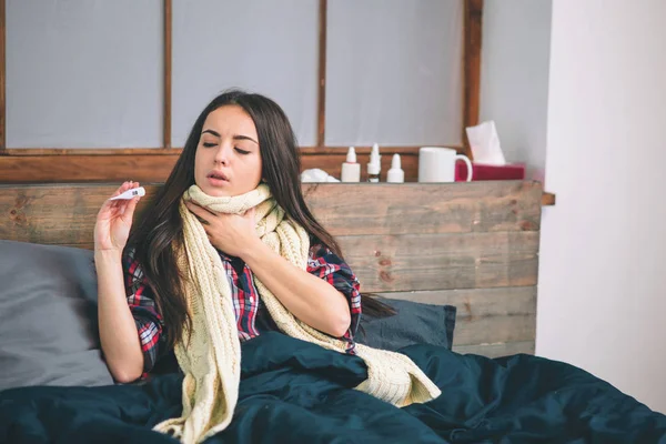 Kobieta z wirusem grypy, leżąc w łóżku, ona jest pomiar jej temperatury z termometru i dotykając jej czoło. — Zdjęcie stockowe