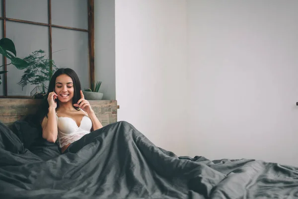 Όμορφη σέξι μελαχρινή γυναίκα ξαπλωμένη στο κρεβάτι μιλάμε στο τηλέφωνο — Φωτογραφία Αρχείου
