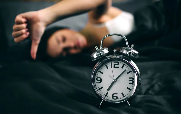 Femeie tânără care doarme și ceas deșteptător în dormitor acasă. Fata a dormit prea mult în pat și se uită la ceas deșteptător în șoc — Fotografie, imagine de stoc