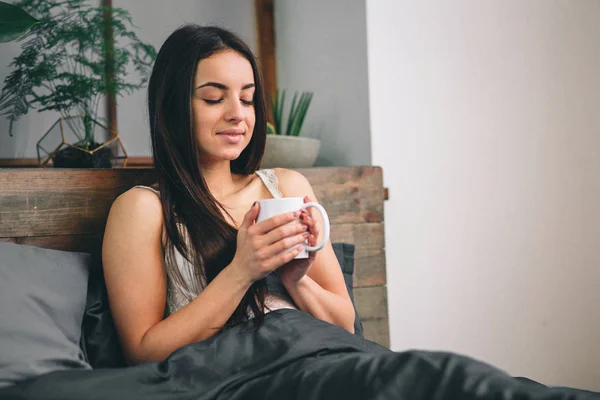 God morgon vaknade kvinna upp i sängen. Kvinna som dricker kaffe i sängen — Stockfoto