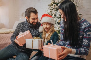 Mutlu Noeller ve mutlu tatil neşeli anne, baba ve sevimli kızı hediye alışverişi. Anne-baba ve küçük çocuk kapalı Noel ağacı yakınındaki eğleniyor. Sabah Xmas. Portre aile
