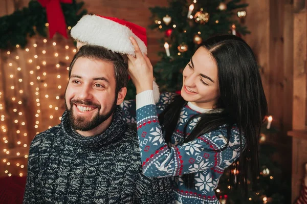 Joyeux Noël et bonne année. Jeune couple célébrant des vacances à la maison. Les femmes habillent un chapeau de Noël sur un homme — Photo