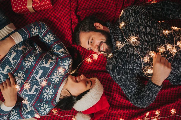 Feliz Navidad y Feliz Año Nuevo. Pareja joven celebrando vacaciones en casa. Mujer y hombre yacen en la alfombra y se miran el uno al otro. Vista superior — Foto de Stock