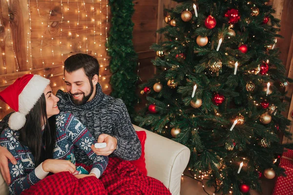 Frohe Weihnachten und ein gutes neues Jahr. junges Paar beim Urlaub zu Hause. Der Mann hält die Fernbedienung vom Fernseher. ein Mann und eine junge Frau schauen fern — Stockfoto
