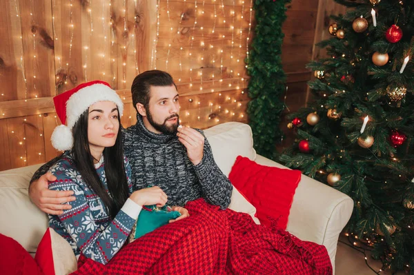 Buon Natale e felice anno nuovo. Giovane coppia che celebra la vacanza a casa. Un ragazzo e una giovane donna stanno guardando la televisione — Foto Stock