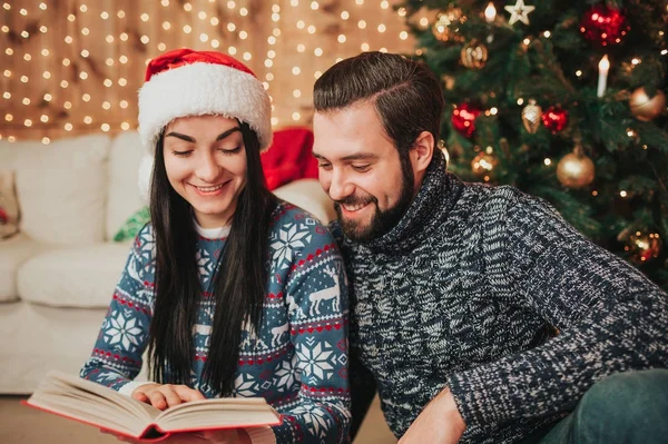 Feliz Navidad y Feliz Año Nuevo. Pareja joven celebrando vacaciones en casa. Un hombre y una mujer están leyendo un libro — Foto de Stock