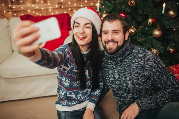 Feliz Navidad y Feliz Año Nuevo. Pareja joven celebrando vacaciones en casa. Hombre y mujer hacen selfie en el teléfono inteligente — Foto de Stock