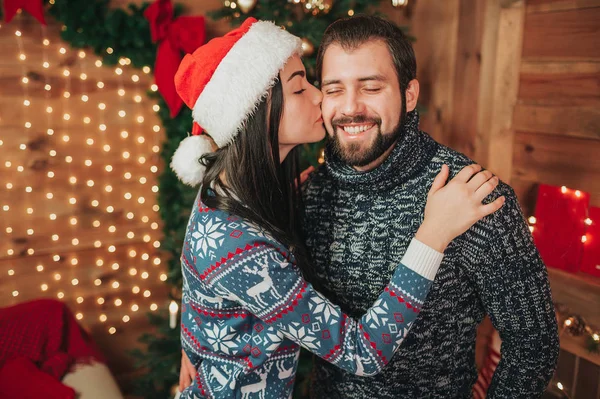 Frohe Weihnachten und ein gutes neues Jahr. junges Paar beim Urlaub zu Hause. eine junge Frau küsst einen jungen bärtigen Mann auf die Wange — Stockfoto