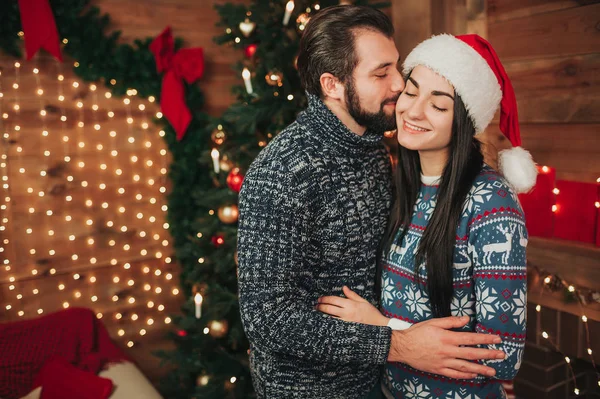 Prettige kerstdagen en gelukkig Nieuwjaar. Jong koppel vieren vakantie thuis. Een jonge man met een baard kussen een jonge vrouw op de Wang. — Stockfoto