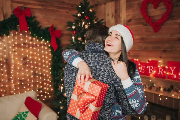 Feliz Navidad y Feliz Año Nuevo. Pareja joven celebrando vacaciones en casa. Feliz joven hombre y mujer abrazan y se dan regalos — Foto de Stock