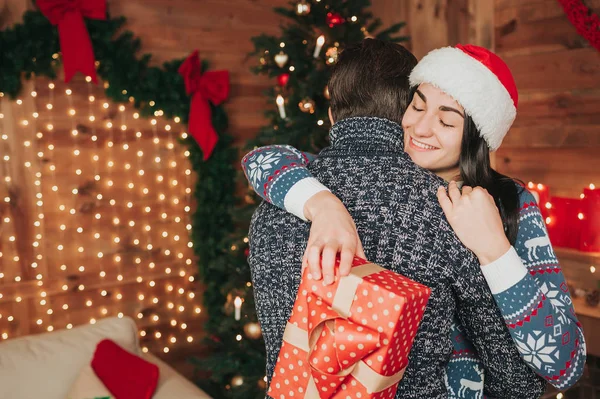 Feliz Navidad y Feliz Año Nuevo. Pareja joven celebrando vacaciones en casa. Feliz joven hombre y mujer abrazan y se dan regalos — Foto de Stock