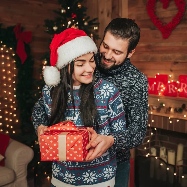 Feliz Navidad y Feliz Año Nuevo. Pareja joven celebrando vacaciones en casa. Feliz joven hombre y mujer abrazan y se dan regalos — Foto de Stock