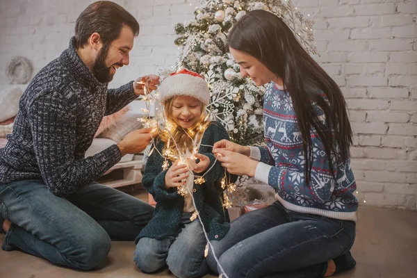 Schöne junge Familie genießt ihre gemeinsame Weihnachtszeit, schmückt den Weihnachtsbaum, arrangiert die Weihnachtsbeleuchtung und hat Spaß — Stockfoto