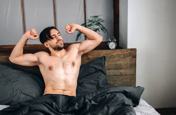 Un tipo despreocupado disfrutando de un nuevo día. Sexy, hombre barbudo feliz en la cama — Foto de Stock