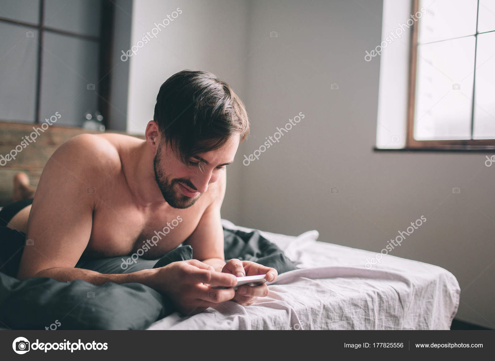 Cheerful Young Man Speaking By Cellphone In Bedroom