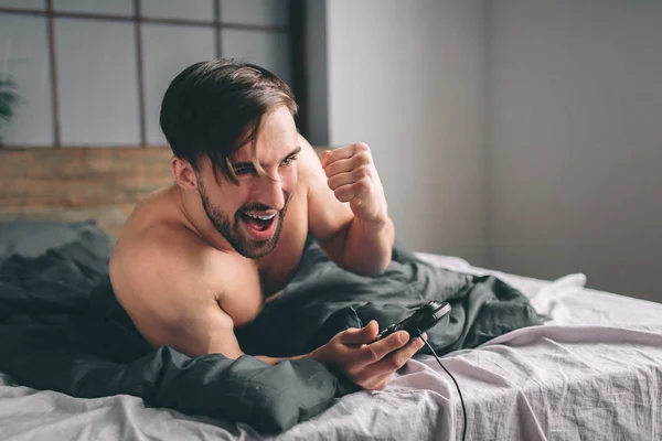 Desnudo barbudo hombre de pelo oscuro que se divierten jugando videojuegos en línea usando joystick — Foto de Stock