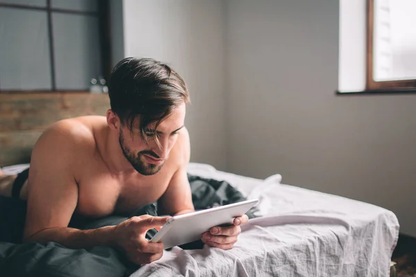 Молодой человек отдыхает на кровати и с помощью цифрового планшета — стоковое фото