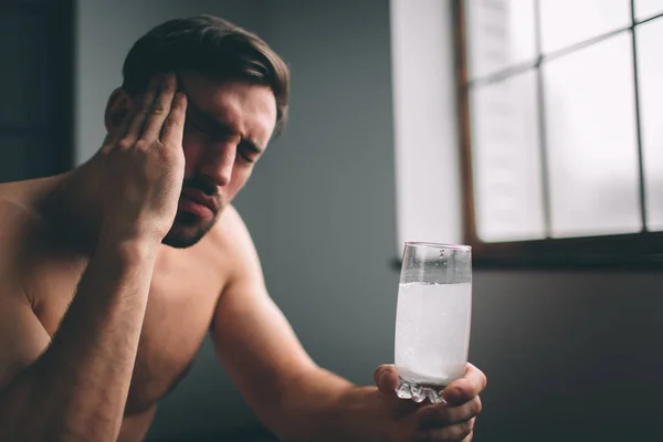 Sad guy suffering from hangover in morning. Naked bearded dark-hair sleepy young man holding a glass of water. — Stock Photo, Image