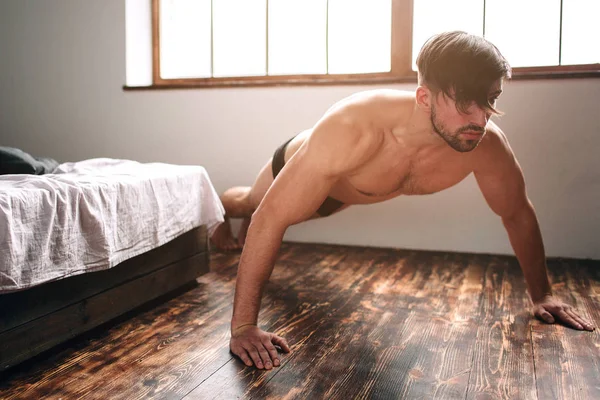 Nu barbudo escuro cabelo homem fazendo push-up exercício casa manhã . — Fotografia de Stock