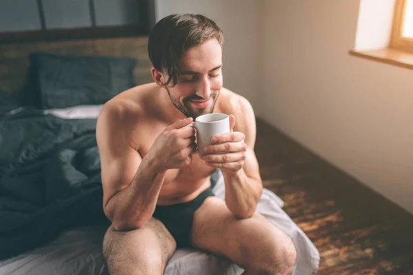 벌 거 벗은 수염된 어두운 머리 잘생긴 남자가 뜨거운 차 또는 그의 침실에 있는 커피 잔을 들고 있다. 그것은 아침 시간. — 스톡 사진