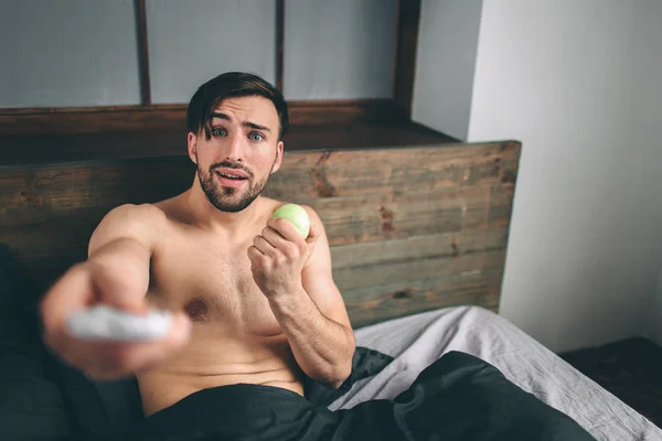 Cabelo escuro barbudo nu assistindo televisão deitada na cama — Fotografia de Stock