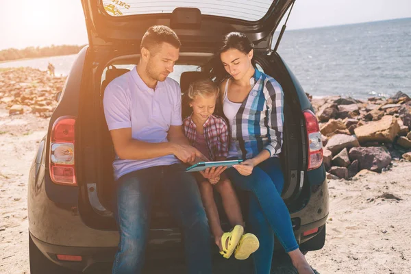 Familia feliz en un viaje por carretera en su coche. Papá, mamá e hija están viajando por el mar o el océano o el río. Paseo de verano en automóvil — Foto de Stock