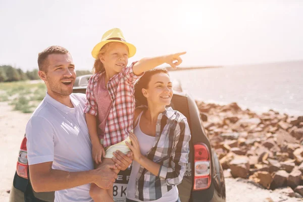 Pareja joven de pie cerca de la bota abierta del coche con maletas y bolsas. Papá, mamá e hija están viajando por el mar o el océano o el río. Paseo de verano en automóvil . — Foto de Stock