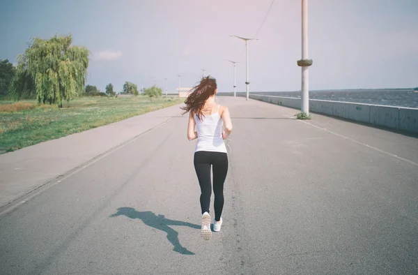 Vacker kvinna kör under solnedgången. Unga fitness modell nära havet. Klädd i sportkläder. — Stockfoto