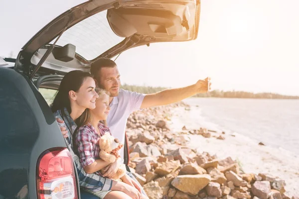 Happy family on a road trip in their car. Dad, mom and daughter are traveling by the sea or the ocean or the river. Summer ride by automobile — Stock Photo, Image
