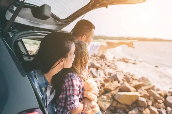 Happy family on a road trip in their car. Dad, mom and daughter are traveling by the sea or the ocean or the river. Summer ride by automobile — Stock Photo, Image