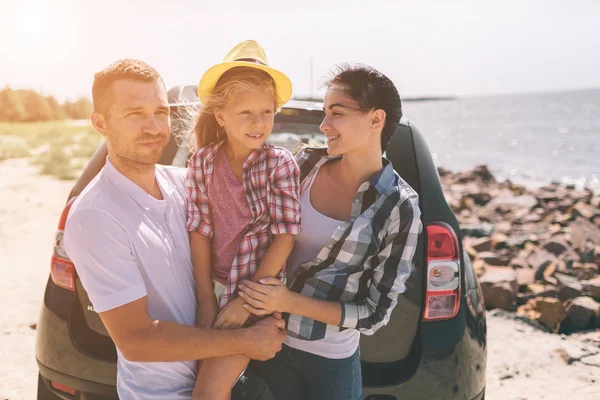 Mladý pár stojící poblíž otevřeného vozu boot s kufry a tašky. Táta, Máma a dcera na cestách do moře nebo oceán nebo na řeku. Letní jízda automobilem. — Stock fotografie
