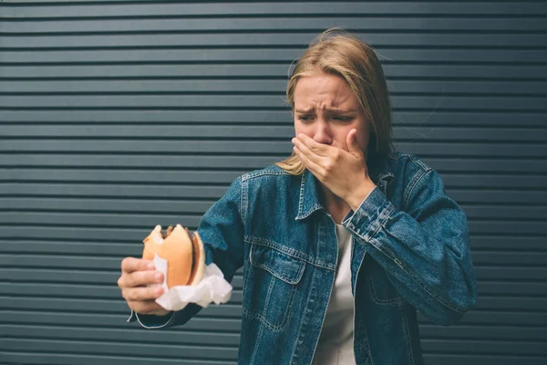 Genç kadın Fast food açık ve bir duygu çok kötü yemek — Stok fotoğraf