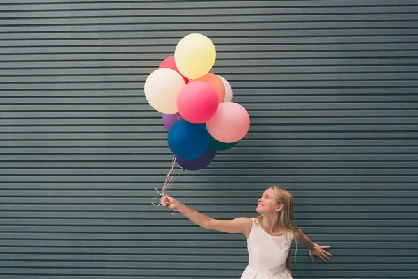 Glad ung kvinna med färgglada ballonger på en gata nära grå - utomhus sommaren koncept — Stockfoto