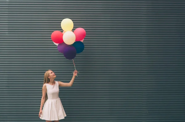 Glad ung kvinna med färgglada ballonger på en gata nära grå - utomhus sommaren koncept — Stockfoto
