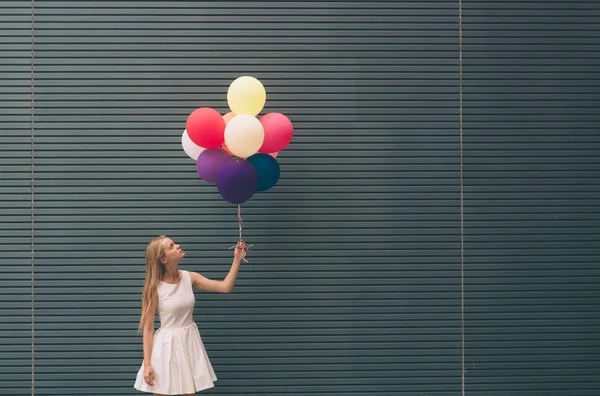 Glad ung kvinna med färgglada ballonger på en gata nära grå väggen - utomhus sommaren koncept — Stockfoto