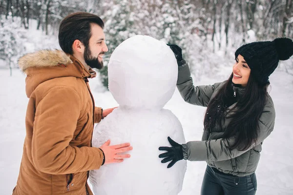 快乐的年轻夫妇在冬天。家庭户外。男人和女人看向上和笑。爱, 乐趣, 季节和人-漫步在冬天公园。做雪人. — 图库照片