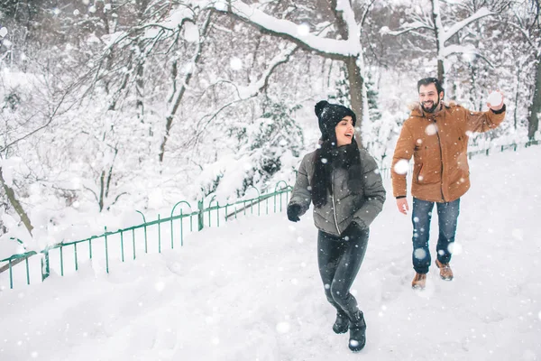 冬の幸せな若いカップル。屋外の家族。男と女の上方への検索と笑っています。愛、喜び、シーズン、冬の公園を歩いて人々。雪だるま式に彼は — ストック写真