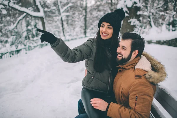 冬の幸せな若いカップル。屋外の家族。男と女の上方への検索と笑っています。愛、喜び、シーズン、冬の公園を歩いて人々。女性モデルは、彼の膝の上に座っています。. — ストック写真