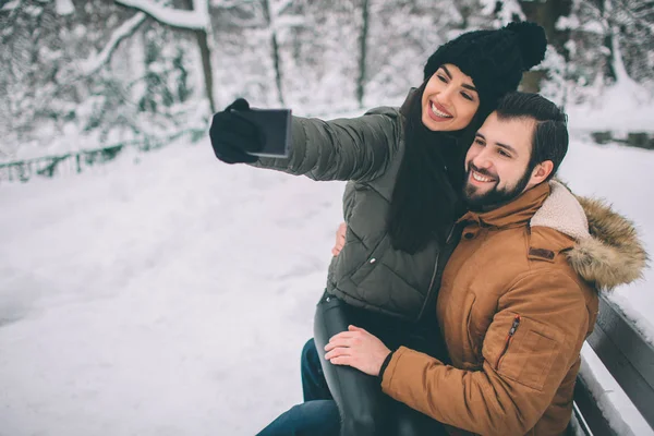 快乐的年轻夫妇在冬天。家庭户外。男人和女人看向上和笑。爱, 乐趣, 季节和人-漫步在冬天公园。他们让自拍 — 图库照片