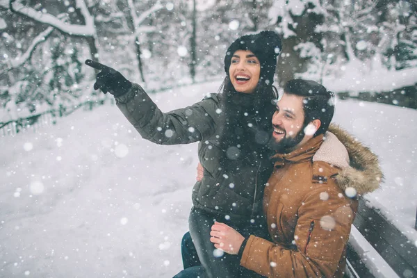 Joyeux jeune couple en hiver. Famille En plein air. homme et femme regardant vers le haut et riant. L'amour, le plaisir, la saison et les gens - marcher dans le parc d'hiver. Femme modèle assis sur ses genoux . — Photo