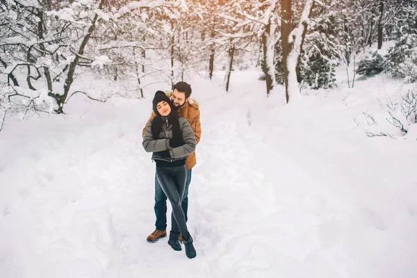 快乐的年轻夫妇在冬天。家庭户外。男人和女人看向上和笑。爱, 乐趣, 季节和人-漫步在冬天公园。下雪了, 他们相拥 — 图库照片