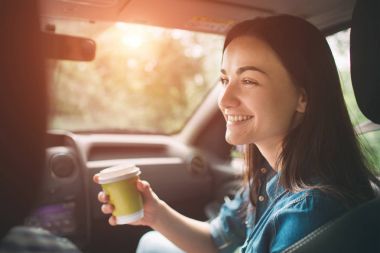 Beautiful woman smiling while sitting on the front passenger seats in the car and she is drinking coffee from a disposable cup clipart