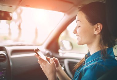 Ön yolcu koltukları arabada otururken gülümseyen güzel kadın. Kız bir akıllı telefon kullanıyor