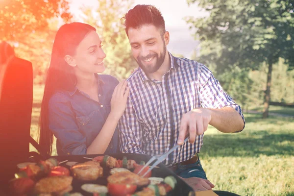 Przyjaciele Dokonywanie grilla i obiad w naturze. Para zabawy podczas jedzenia i picia na piknik - szczęśliwi ludzie grill party. — Zdjęcie stockowe